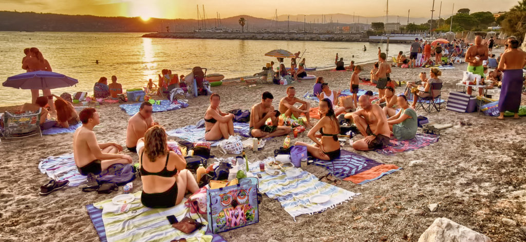 Groupe d'amis Yepengo en maillot de bain sur une plage de sable niçoise sous un coucher de soleil